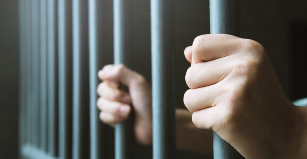 Zwei Hände, die zwei Gitterstäbe einer Gefängnistür umschließen