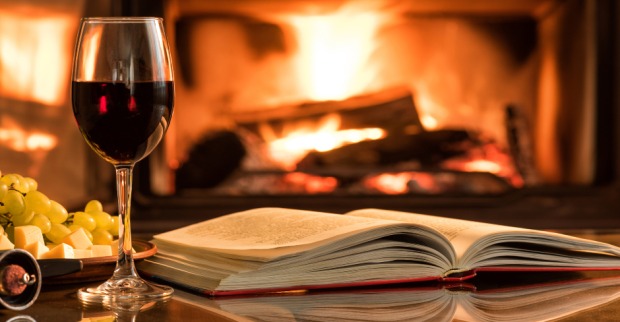 Lesestunde am offenen Kamin mit einem Glas Rotwein | Credit: iStock.com/Rasulovs
