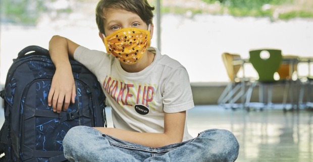 Ein etwa 10jähriger Schüler mit Stoffmaske sitzt in der Aula einer Schule