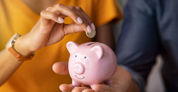 Paar hält gemeinsam ein Sparschwein, in das sie eine Münze einwirft | Credit: iStock.com/Ridofranz