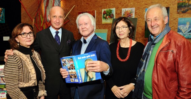Arno Wiedergut steht mit seinem Buch in der Hand inmitten von Besuchern seiner Buchpräsentation
