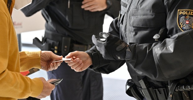 Ausschnitt, Mann übergibt einem uniformierten Polizisten Impfausweis