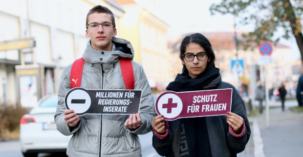 Ein junger Mann und eine junge Frau halten zwei Schilder mit Botschaften für mehr Gewaltschutz für Frauen in die Kamera