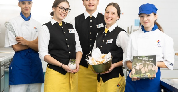 Schüler des CHS-Villach in eleganter Gastro-Montur halten ein Kochbuch und einen Brotkorb in die Kamera
