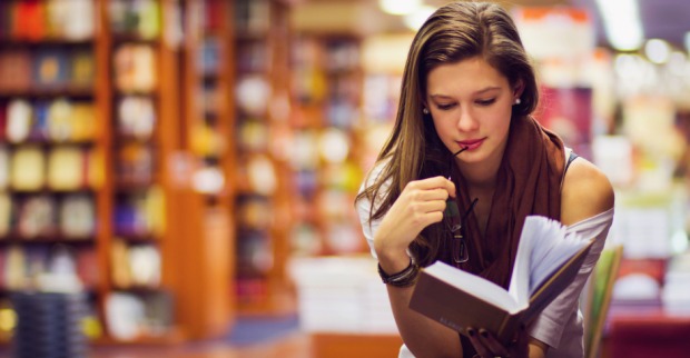 Junge Frau, vertieft in ihr Buch, in einer Buchhandlung | Credit: iStock.com/orbandomonkos