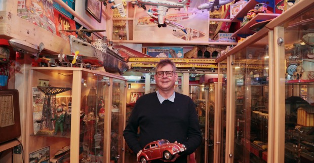 Johannes Krämmer steht mit einem Spielzeugauto in der Hand vor meterhohen Vitrinen mit unzähligen Spielzeugexponaten