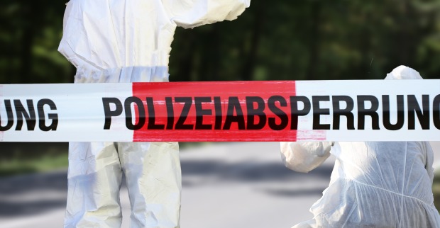 Zwei Mitarbeiter der Spurensicherung in weißen Overalls hinter einer Polizeiabsperrung
