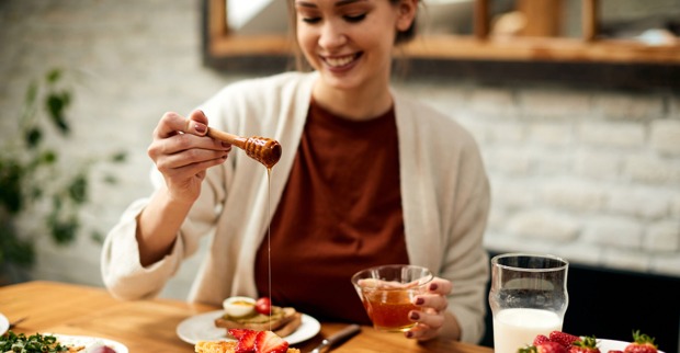 Junge Frau süßt mit Honig ihr Frühstück | Credit: iStock.com/Drazen Zigic