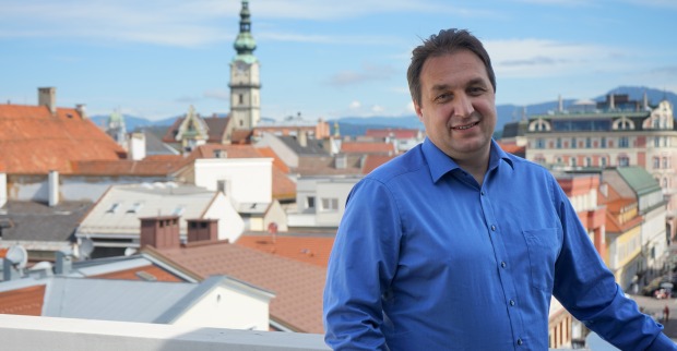 Jürgen Hartinger auf dem Balkon des obersten Stockwerks der KLV-Zentrale vor der Kulisse der Klagenfurter Innenstadt
