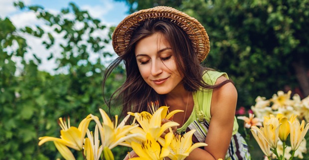 Junge Frau mit Sommerhut riecht an den blühenden Lilien in ihrem Garten | Credit: iStock.com/Maryviolet