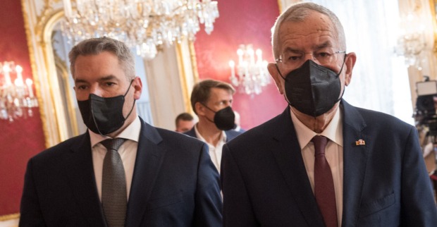 Bundeskanzler Karl Nehammer hinter Bundespräsident Alexander Van der Bellen in der Hofkanzlei. Beide tragen eine schwarze FFP2-Maske