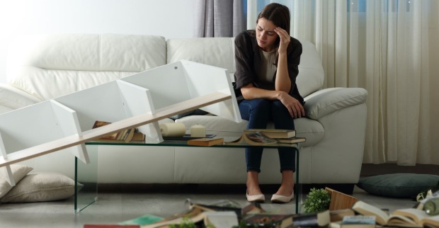 Frau sitzt traurig auf der Couch in der ausgeraubten Wohnung | Credit: iStock.com/AntonioGuillem
