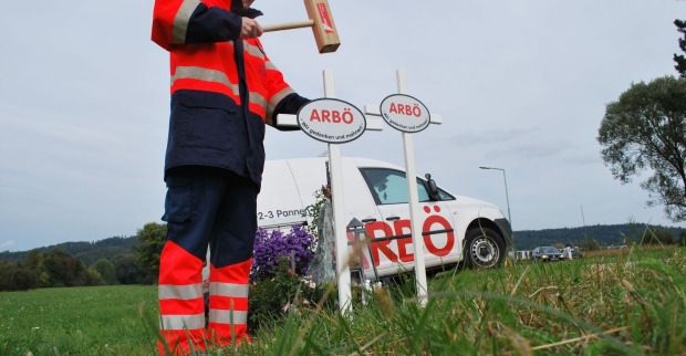 Mann bringt mit Hammer weiße Kreuze an Straßenrändern an