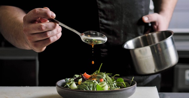 Nahaufnahme eines Küchenchefs, der Soße auf eine Salatschale gießt