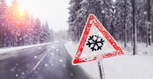 Ein Warnschild, das eine Schneeflocke zeigt, vor einer tiefverschneiten Waldstraße