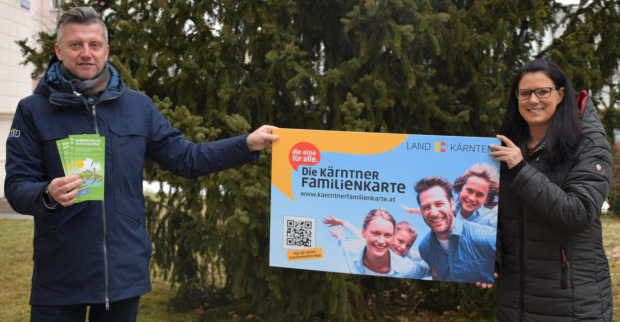 Sara Schaar und Anton Fasching halten vor einem Baum im Garten der Landesregierung das überdimensional große Modell einer Kärnten Card in die Höhe