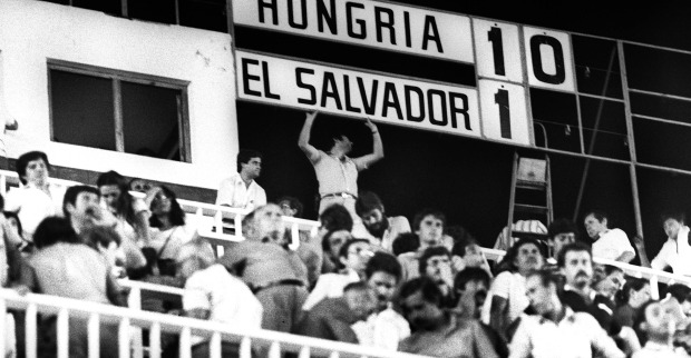 Schwarz-Weiß-Aufnahme der Publikumsränge in der Partie Ungarn - El Salvador. Im Hintergrund ist die Anzeigentafel zu sehen, die das Resultat 10:1 aufweist