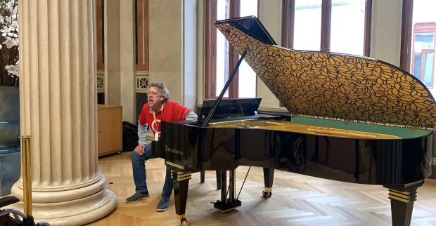 Ein älterer Mann in roten T-Shirt am Hocker des Flügels im Parlament