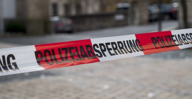 Ein rot-weiß-rotes Absperrband mit dem Schriftzug "Polizeiabsperrung" auf eine Straße mit Kopfsteinpflaster.