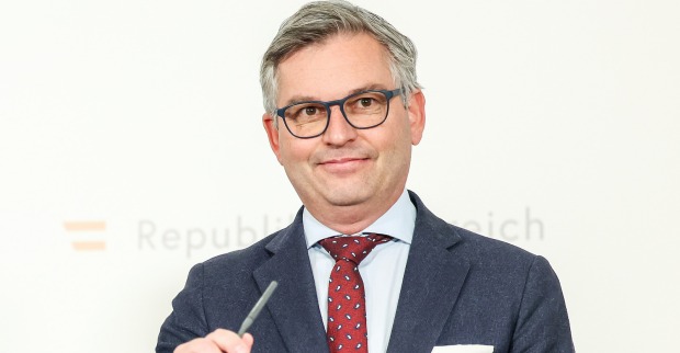 Magnus Brunner vor der Pressewand des FInanzminiteriums. Er grinst schelmisch