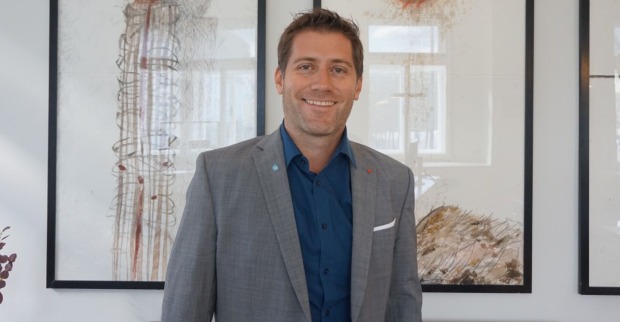 Philipp Liesnig, der ein graues Sakko mit blauem Hemd trägt und vor einem modernen Kunstwerk steht
