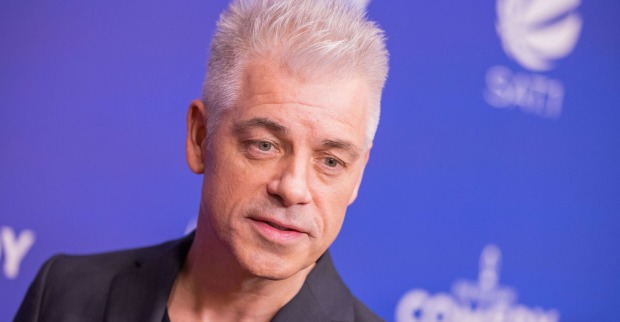 Ein Mann steht vor blauem Hintergrund und hat weiße Haare.