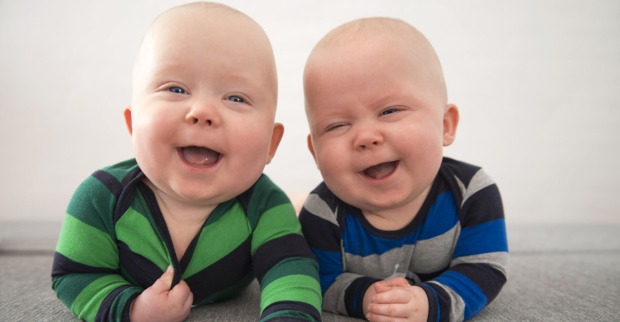 Zwei Babys liegen am Bauch und lachen in die Kamera.