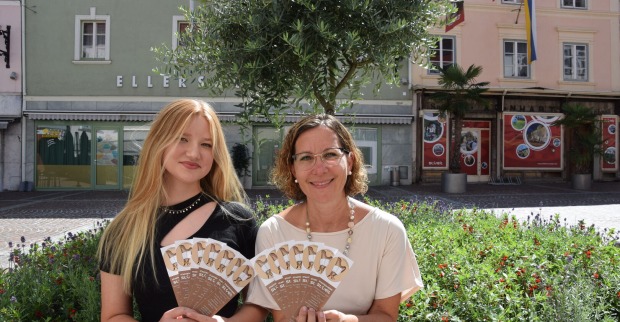 Zwei Frauen sitzen im Freien auf der Bank und halten Flyer in der Hand.