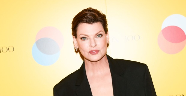 Linda Evangelista mit kurzen Haaren und einem schwarzen Anzug vor einer gelben Wand