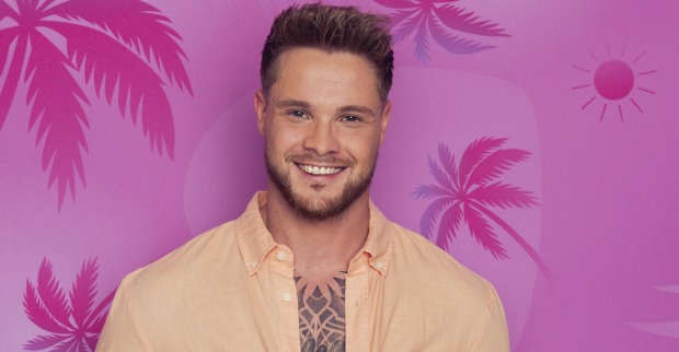 Daniel Love Island mit einem gelben offenen Hemd vor einer pinken Wand.