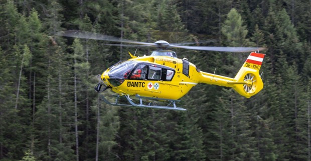 Der gelbe ÖAMTC-Hubschrauber fliegt in einem Waldgebiet.