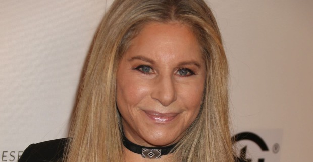 Barbara Streisand mit einer engen schwarzen Kette und offenen blonden Haaren vor einer Fotoleinwand.