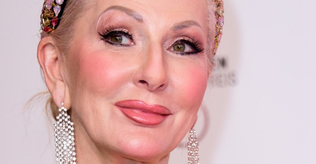 Désirée Nick mit einem starken Make Up vor einer Leinwand mit geschlossenen Haaren und großen silber Ohrringen.