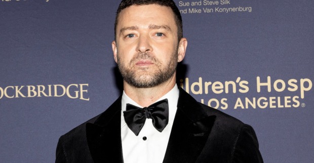 Justin Timberlake trägt einen schwarzen Suite und kurze Haare vor einer Fotoleinwand.