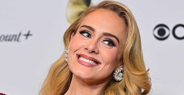 Adele trägt eine voluminöse Föhnfrisur und blonde Haare. Sie ist stark geschminkt im Red-Carpet Look und grinst in die Kamera. Sie trägt auffallende Diamantohrringe.