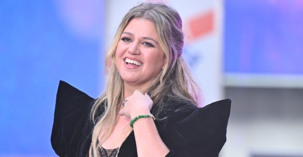 Kelly Clarkson trägt ein schwarzes Kleid und halb geschlossene blonde Haare. Sie lächelt in die Ferne.