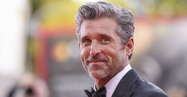 Patrick Dempsey hat graue kurze Haare, einen schwarzen Anzug und ein weißes Hemd. Er blickt von der Seite in die Kamera.