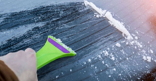 Eis wird mit einem Eiskratzer von der Scheibe entfernt.