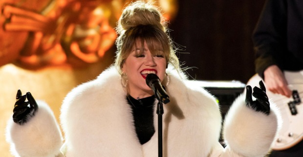 Kelly Clarkson trägt einen weißen Pelzmantel und steht auf einer Bühne.