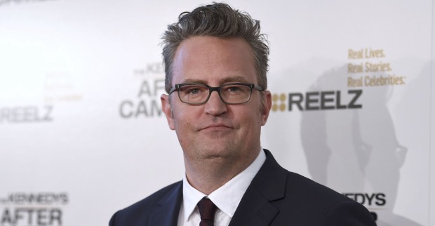 Matthew Perry vor einer Fotoleinwand mit einem Sakko.