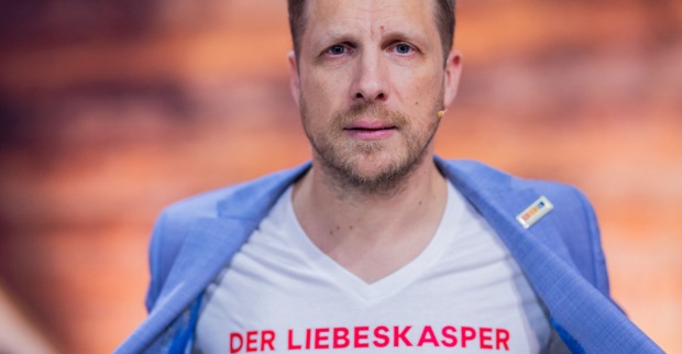 Oliver Pocher mit einem weißen T-Shirt auf dem steht "Liebeskasper" und einem hellblauen Sakko.