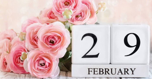 Übereinander gestapelte weiße Holzklötze, die zusammengesetzt den "29. Februar" ergeben, verziert mit rosa Rosen.