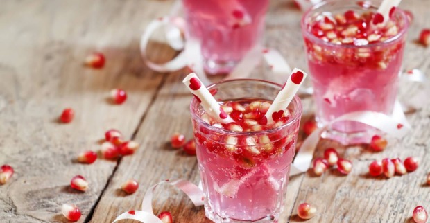 Rosafarbene Cocktails für den Valentinstag, verziert mit Granatapfelkernen und herzförmigen Zuckerstangen
