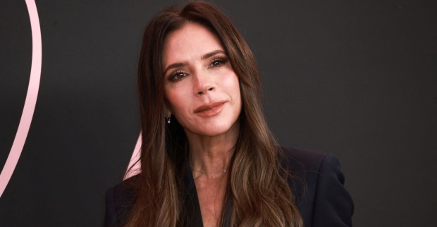 Victoria Beckham mit langen braunen Haaren und einem schwarzen Outfit vor einer schwarzen Fotowand.