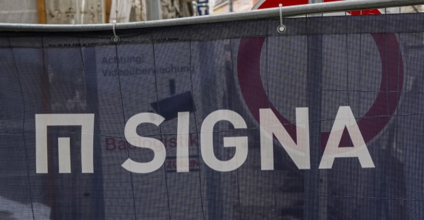 Eine Bauplane mit Logo und Schriftzug der Signa, dahinter ein Stoppschild