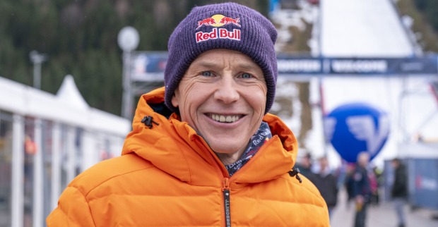 Ein Mann in oranger Skijacke und mit "Red Bull"-Haube steht vor einer Skipiste