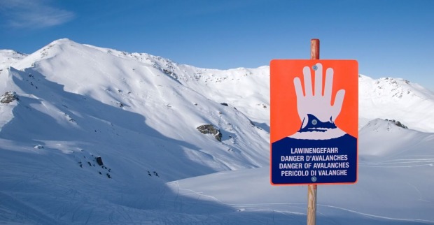Hinweisschild für Lawinengefahr vor verschneiten Bergen.