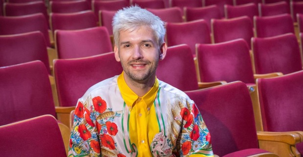 Michi Buchinger mit einem bunten T-Shirt auf einer Sitzreihe.