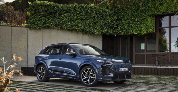 Ein blau glänzender Audi Q6 e-tron steht auf einer Terrasse. Im Hintergrund sind Efeuranken, ein Tisch und Sesseln zu sehen.