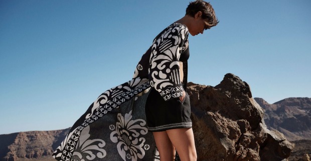 Model mit flatterndem Mantel und Shorts vor Felsenkulisse